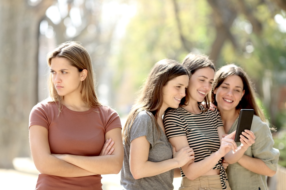 Blonde woman turns her back to a group of women looking on the phone