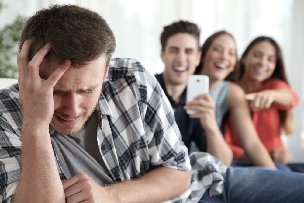 Distressed man feeling everyone hates him with laughing people in the background