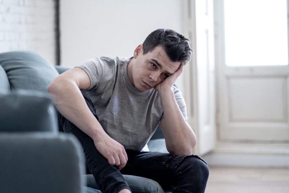 Man sitting on the couch wondering if he is tired or depressed