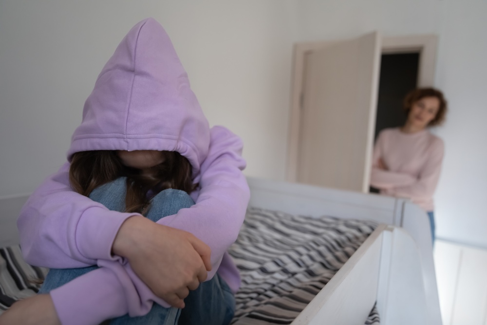 Female teen wearing a violet hoodie with her mother checking on her