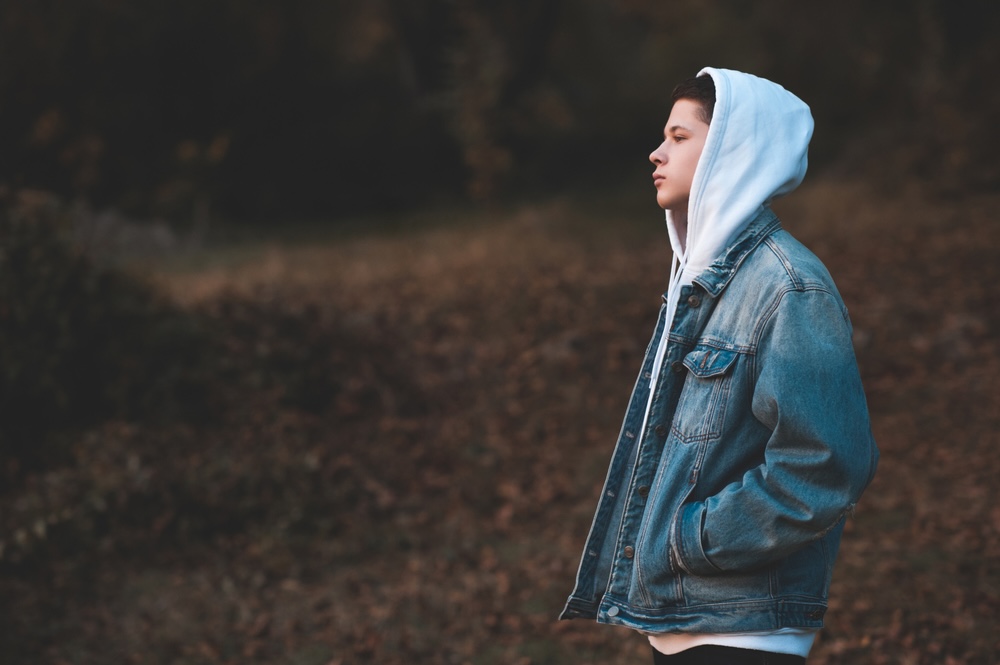 Male teenager wearing a blue hoodie standing outdoors