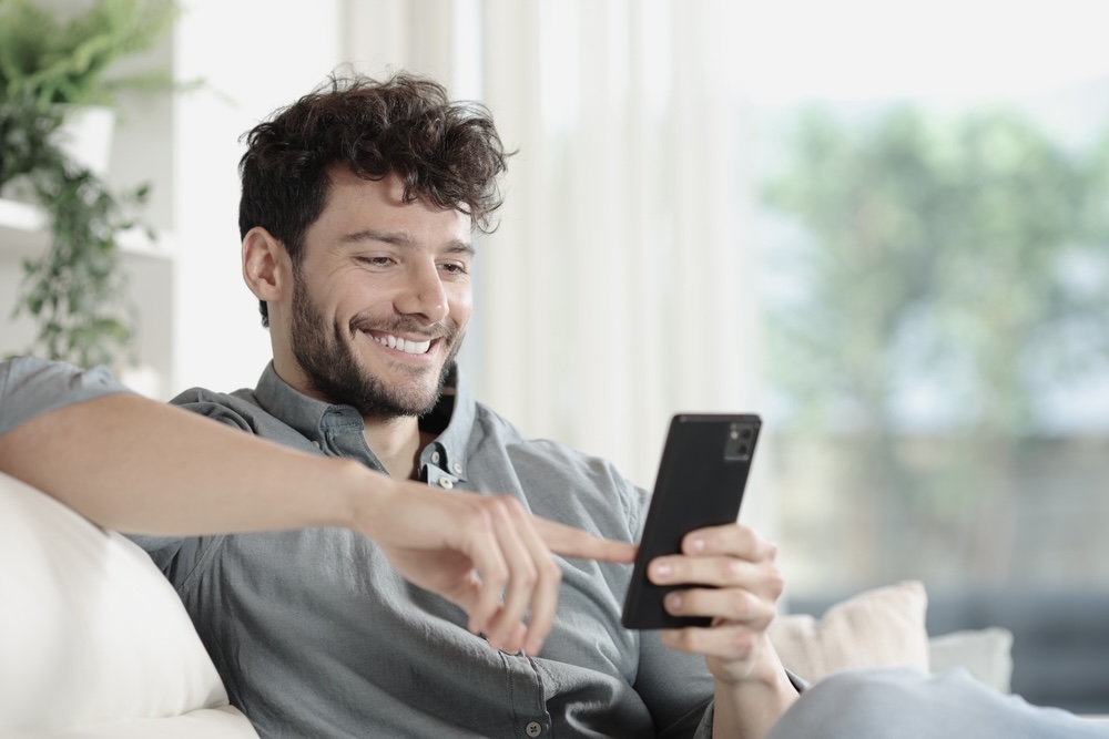 Man smiling while reading positive mental health quotes on his mobile phone